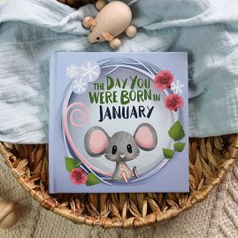 The book cover for Day You Were Born In January in a seagrass tray. A playful, illustrated mouse sat down surrounded by seasonal flowers and snowflakes.